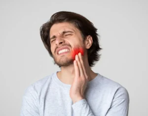 Blog 86 Man wincing and pressing a hand against his sore jaw, with the painful area highlighted in red