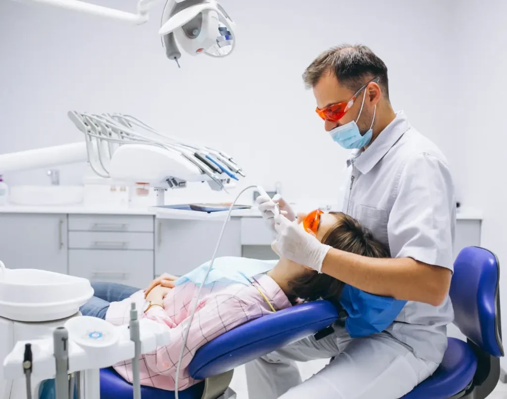Dentist wearing orange safety glasses examining a patient's teeth in a dental chair